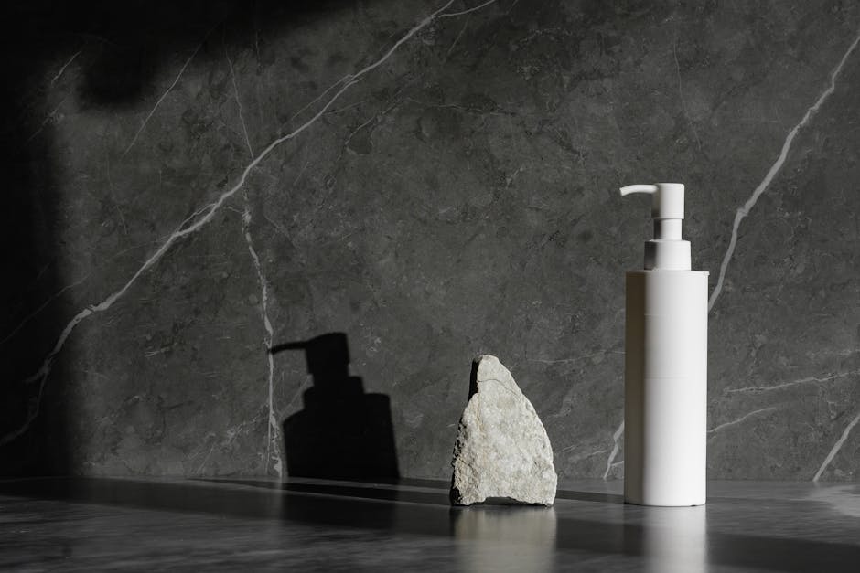 Sleek white pump bottle beside a rock on a marble surface with dramatic lighting.