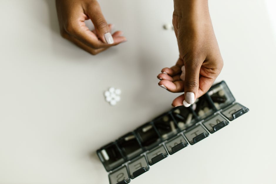 Close-up of hands placing pills into a weekly pill organizer, symbolizing health and medication management.
