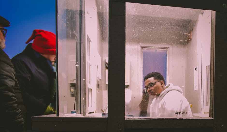 Man in white hoodie inside a glass booth at night, interacting thoughtfully.