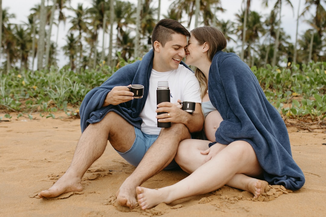 A man and woman sitting on a beach under a blanket