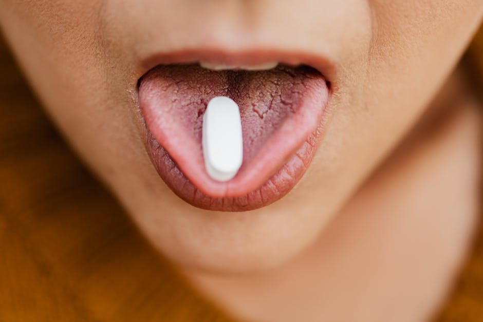 Close-up image of a person placing a pill on their tongue, symbolizing medication or health care.