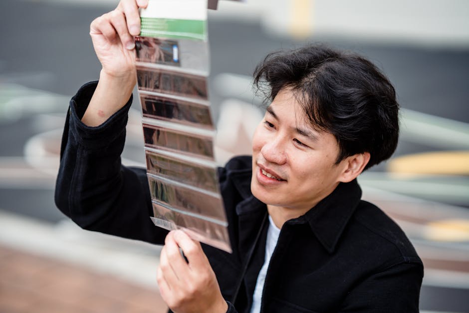 Smiling man holds and examines film strips, showcasing passion for photography.