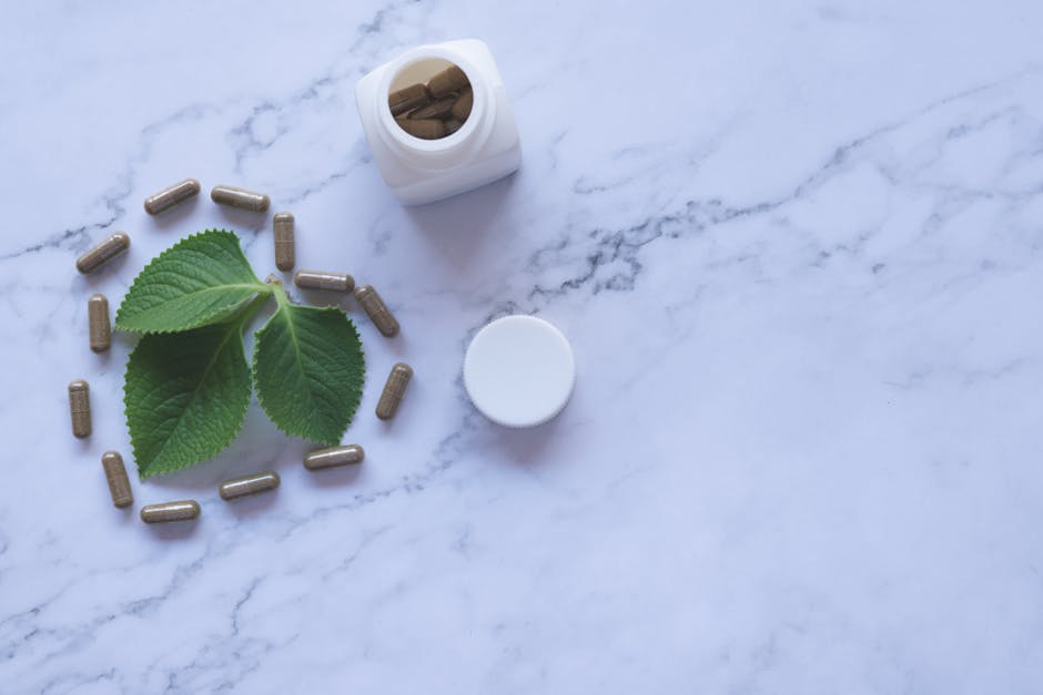 Flat lay of herbal capsules, leaves, and bottle on marble surface, symbolizing natural wellness.