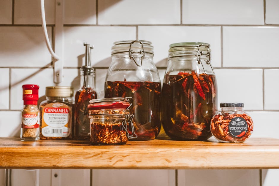 A rustic display of chili-infused oils and spices in jars on a kitchen shelf.
