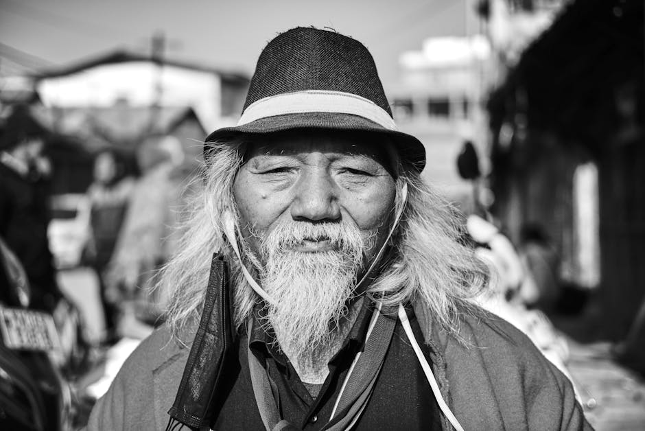 Close-up black and white portrait of a senior man with a hat and gray beard.