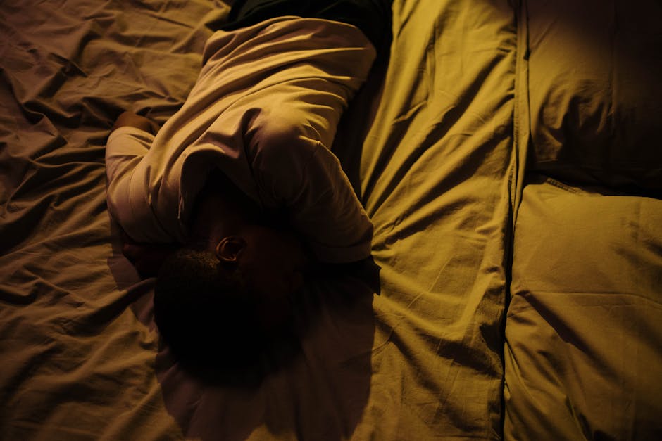 A man in white shirt lying on bed in a dimly lit room, displaying tranquility.