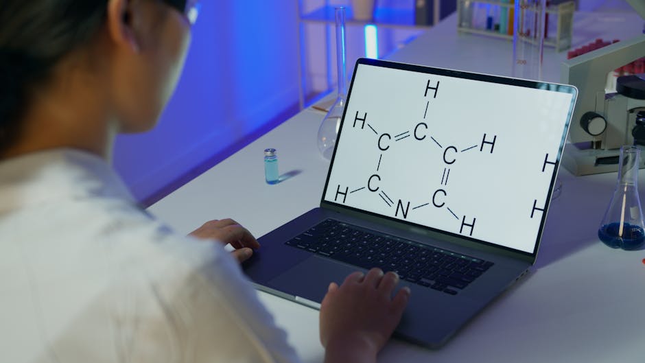 A scientist reviews a chemical formula on a laptop in a laboratory setting.