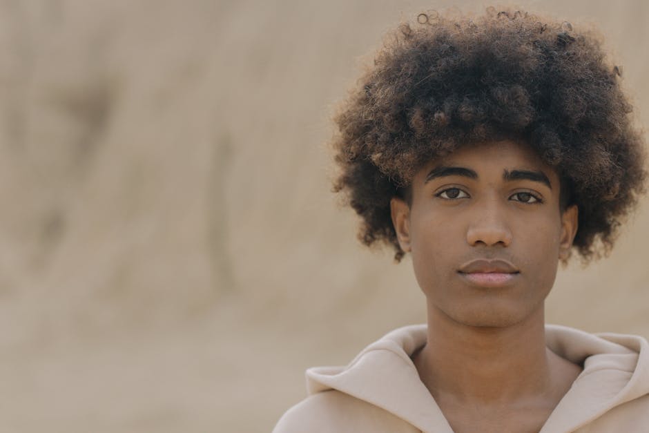 A close-up portrait of a young man with an afro hairstyle, looking confidently at the camera outdoors.