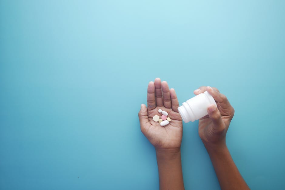 Hands pouring pills from a bottle on a blue background, representing healthcare and medication.