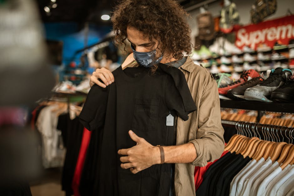 A man wearing a mask selects clothes in an indoor fashion store.