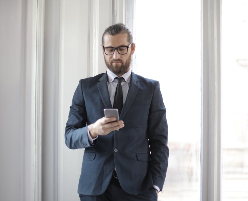 Confident man in formal suit using smartphone by window in office setting.