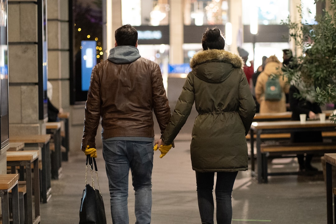 man in brown jacket and blue denim jeans walking on sidewalk during daytime