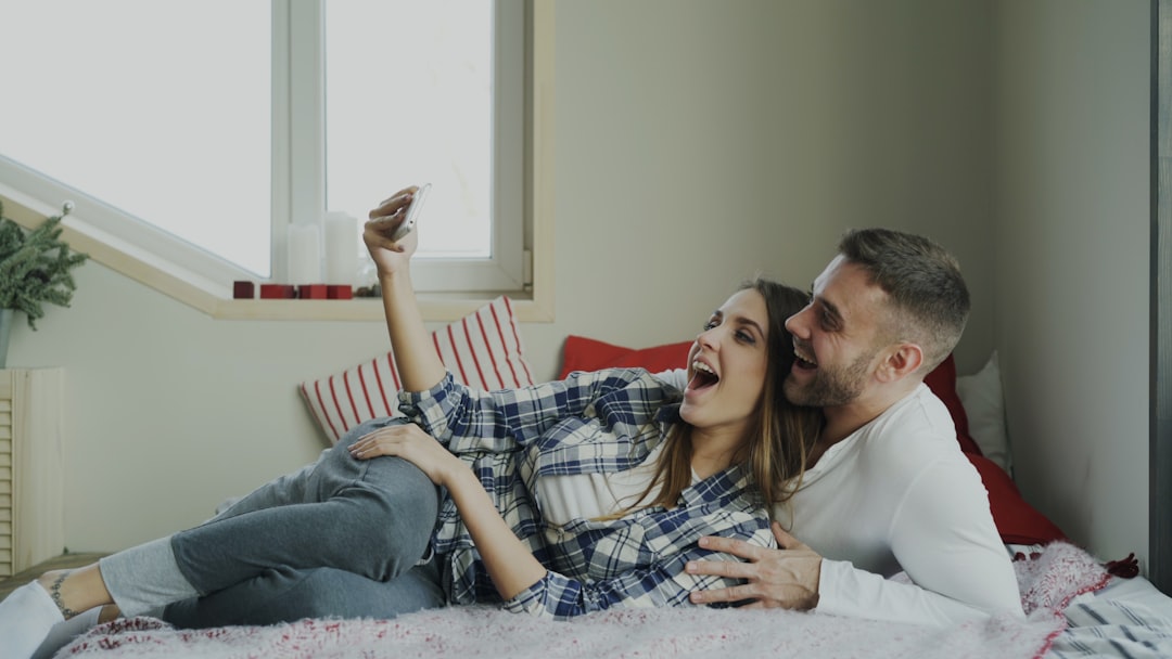 Couple taking a selfie while lying on a bed.