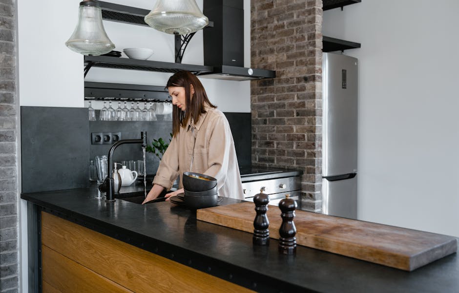 Young woman washing dishes in a contemporary kitchen setting with brick accents.