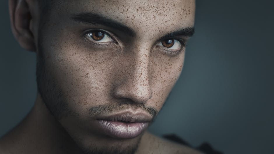 Close-up portrait highlighting the intense gaze of a freckled man with dark eyes, captured in a soft, muted setting.