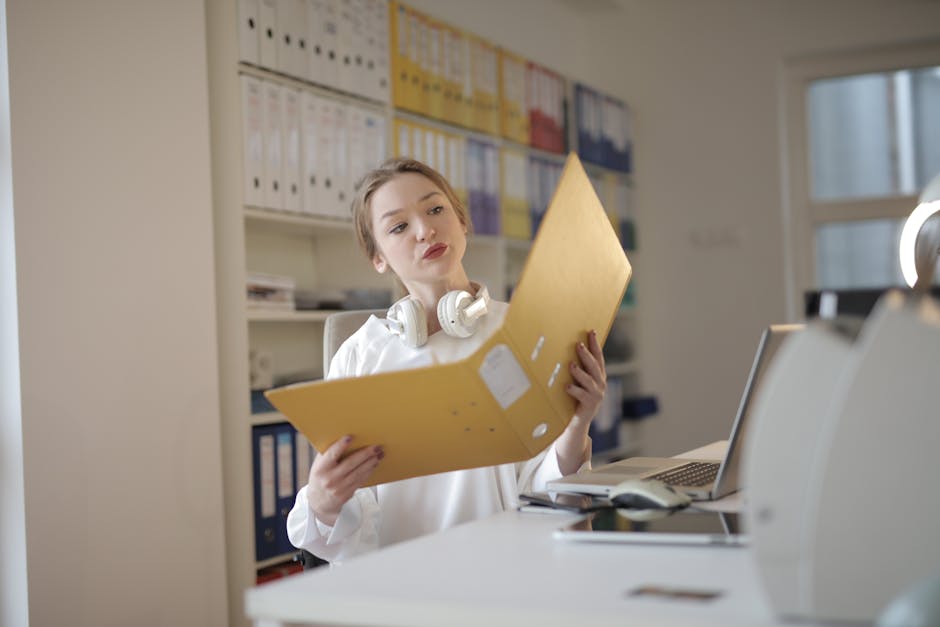 A young woman analyzing documents with concentration in a modern office setting, surrounded by folders and technology.